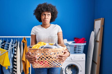 Photo for Black woman with curly hair holding laundry basket skeptic and nervous, frowning upset because of problem. negative person. - Royalty Free Image