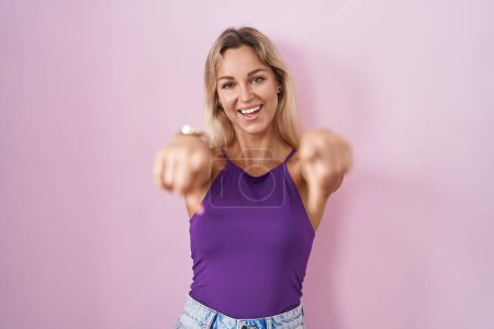 Téléchargez les photos : Jeune femme blonde debout sur fond rose pointant vers vous et la caméra avec les doigts, souriant positif et joyeux - en image libre de droit