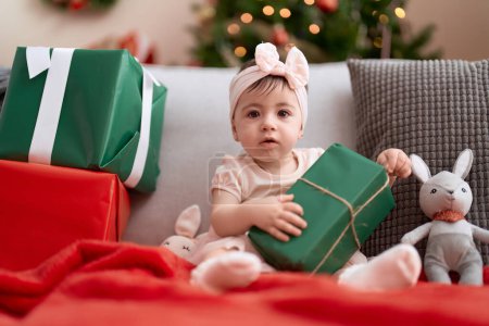 Photo for Adorable toddler opening christmas gift sitting on sofa at home - Royalty Free Image