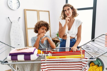 Photo for Young woman and son doing laundry at clothesline serious face thinking about question with hand on chin, thoughtful about confusing idea - Royalty Free Image