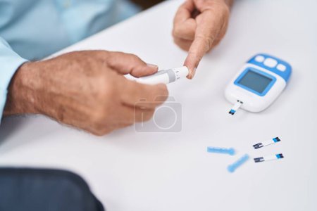 Téléchargez les photos : Senior grey-haired man measuring glucose sitting on table at home - en image libre de droit