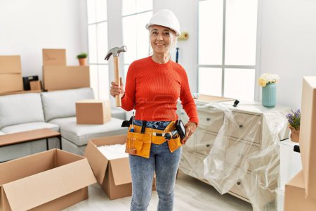Photo for Middle age grey-haired woman repairing holding hammer at new home - Royalty Free Image