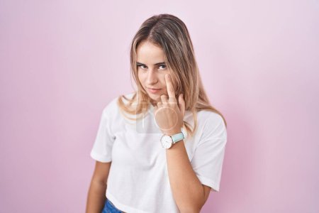 Photo for Young blonde woman standing over pink background pointing to the eye watching you gesture, suspicious expression - Royalty Free Image