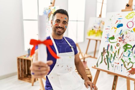 Photo for Young hispanic man smiling confident holding diploma at art studio - Royalty Free Image