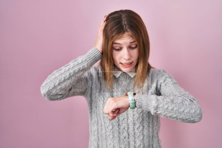 Téléchargez les photos : Beautiful woman standing over pink background looking at the watch time worried, afraid of getting late - en image libre de droit
