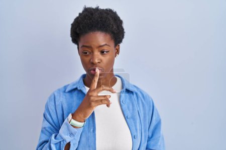 Téléchargez les photos : African american woman standing over blue background asking to be quiet with finger on lips. silence and secret concept. - en image libre de droit