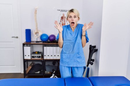 Téléchargez les photos : Young physiotherapist woman working at pain recovery clinic celebrating crazy and amazed for success with arms raised and open eyes screaming excited. winner concept - en image libre de droit