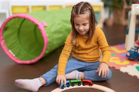 Téléchargez les photos : Adorable fille hispanique jouer avec des voitures jouet assis sur le sol à la maternelle - en image libre de droit