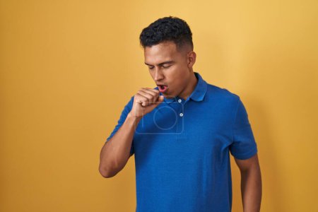 Téléchargez les photos : Jeune homme hispanique debout sur fond jaune se sentant mal et toussant comme symptôme de rhume ou de bronchite. concept de soins de santé. - en image libre de droit