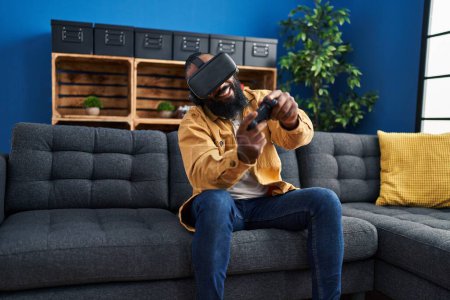 Foto de Joven afroamericano jugando videojuego usando gafas de realidad virtual en casa - Imagen libre de derechos