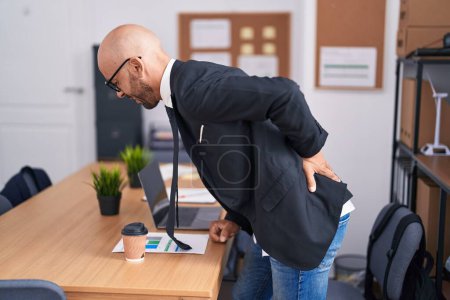 Foto de Joven hombre calvo trabajador de negocios que sufre de dolor de espalda en la oficina - Imagen libre de derechos
