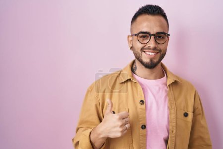 Téléchargez les photos : Young hispanic man standing over pink background doing happy thumbs up gesture with hand. approving expression looking at the camera showing success. - en image libre de droit