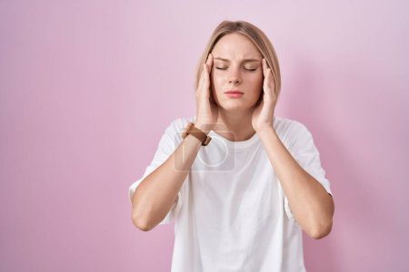 Foto de Young caucasian woman standing over pink background with hand on head, headache because stress. suffering migraine. - Imagen libre de derechos