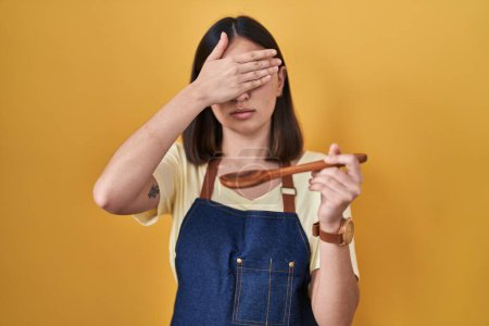 Photo for Hispanic girl eating healthy  wooden spoon covering eyes with hand, looking serious and sad. sightless, hiding and rejection concept - Royalty Free Image