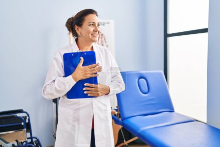 Téléchargez les photos : Middle age hispanic woman physiotherapist holding clipboard at rehab clinic - en image libre de droit
