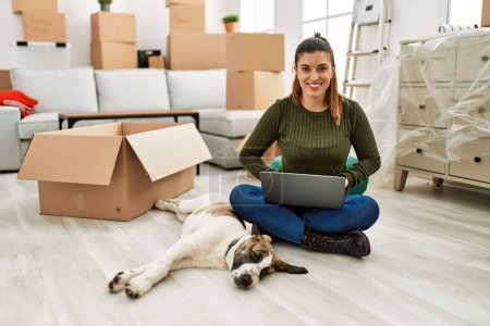 Téléchargez les photos : Jeune femme utilisant un ordinateur portable assis sur le sol avec chien à la maison - en image libre de droit
