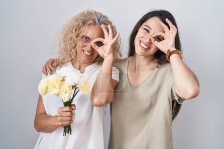 Photo for Mother and daughter holding bouquet of white flowers doing ok gesture with hand smiling, eye looking through fingers with happy face. - Royalty Free Image