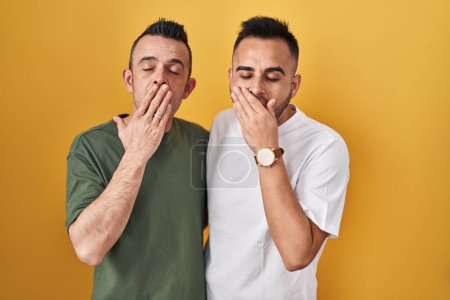 Foto de Homosexual couple standing over yellow background bored yawning tired covering mouth with hand. restless and sleepiness. - Imagen libre de derechos