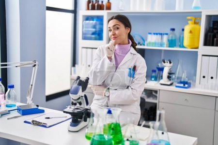 Photo for Young brunette woman working at scientist laboratory serious face thinking about question with hand on chin, thoughtful about confusing idea - Royalty Free Image