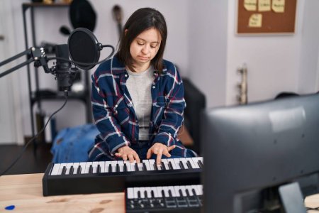 Foto de Mujer joven con síndrome de Down músico tocando el teclado de piano en el estudio de música - Imagen libre de derechos