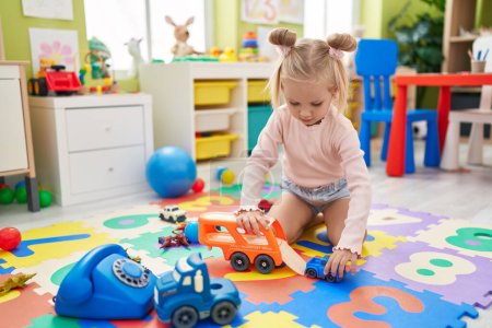 Photo for Adorable caucasian girl playing with cars toy sitting on floor at kindergarten - Royalty Free Image