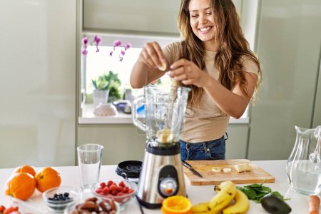 Téléchargez les photos : Jeune belle femme hispanique préparant smoothie aux légumes avec mélangeur à la cuisine - en image libre de droit