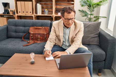 Foto de Hombre de mediana edad que tiene sesión de psicología utilizando la escritura portátil en el cuaderno en la clínica - Imagen libre de derechos