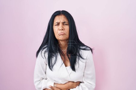Photo for Mature hispanic woman standing over pink background with hand on stomach because indigestion, painful illness feeling unwell. ache concept. - Royalty Free Image