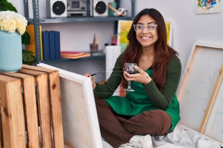 Photo for Young hispanic woman artist drawing and drinking wine at art studio - Royalty Free Image