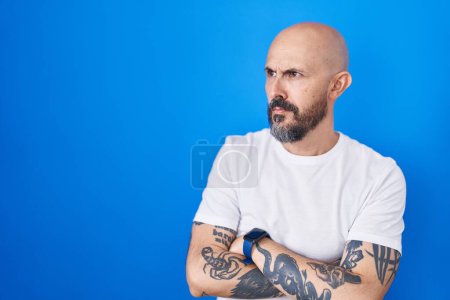 Téléchargez les photos : Hispanic man with tattoos standing over blue background looking to the side with arms crossed convinced and confident - en image libre de droit