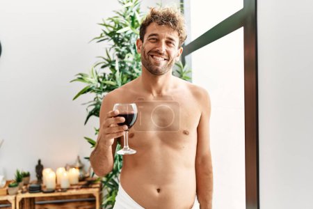 Téléchargez les photos : Jeune homme hispanique souriant boire du vin avec confiance au centre de beauté - en image libre de droit