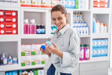 Photo for Young woman customer smiling confident holding deodorant bottles at pharmacy - Royalty Free Image
