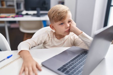 Photo for Adorable toddler student boring using laptop sitting on table at classroom - Royalty Free Image