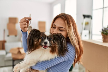 Photo for Young caucasian woman holding key kissing dog at new home - Royalty Free Image
