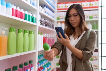 Téléchargez les photos : Jeune asiatique femme client faire photo par smartphone à la bouteille de médecine à la pharmacie - en image libre de droit