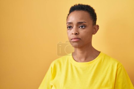 Téléchargez les photos : Femme afro-américaine debout avec une expression sérieuse sur fond jaune isolé - en image libre de droit