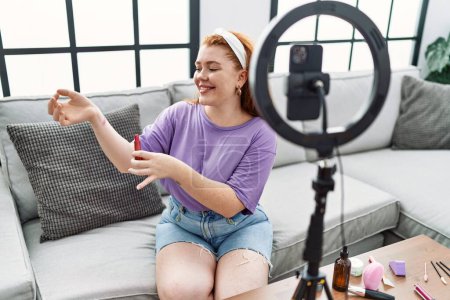 Téléchargez les photos : Jeune rousse femme faisant tutoriel maquillage en utilisant smartphone à la maison - en image libre de droit