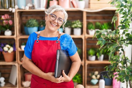Photo for Middle age grey-haired woman florist smiling confident holding binder at florist - Royalty Free Image