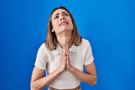 Photo for Hispanic woman standing over blue background begging and praying with hands together with hope expression on face very emotional and worried. begging. - Royalty Free Image