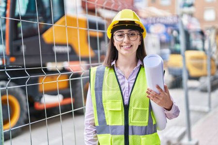 Photo for Hispanic girl wearing architect hardhat at construction site looking positive and happy standing and smiling with a confident smile showing teeth - Royalty Free Image