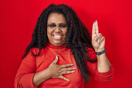 Téléchargez les photos : Plus size hispanic woman standing over red background smiling swearing with hand on chest and fingers up, making a loyalty promise oath - en image libre de droit