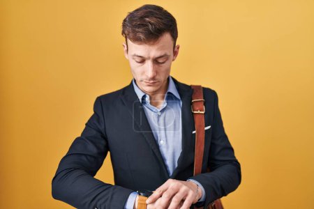 Téléchargez les photos : Homme d'affaires caucasien sur fond jaune vérification de l'heure sur montre-bracelet, détendu et confiant - en image libre de droit