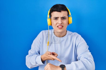 Photo for Non binary person listening to music using headphones in hurry pointing to watch time, impatience, upset and angry for deadline delay - Royalty Free Image