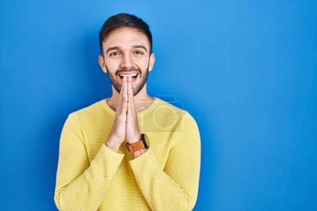 Photo for Hispanic man standing over blue background praying with hands together asking for forgiveness smiling confident. - Royalty Free Image