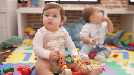 Téléchargez les photos : Deux tout-petits jouant avec des jouets assis sur le sol à la maternelle - en image libre de droit