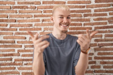 Photo for Young caucasian man standing over bricks wall pointing fingers to camera with happy and funny face. good energy and vibes. - Royalty Free Image