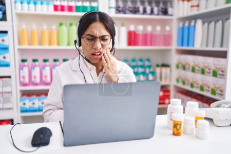 Téléchargez les photos : Young arab woman working at pharmacy drugstore using laptop touching mouth with hand with painful expression because of toothache or dental illness on teeth. dentist - en image libre de droit
