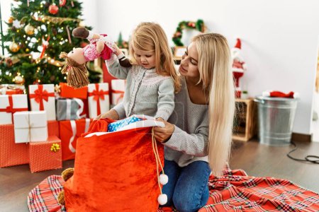 Téléchargez les photos : Mère et fille tenant des cadeaux sur le sac de Noël assis sur le sol à la maison - en image libre de droit