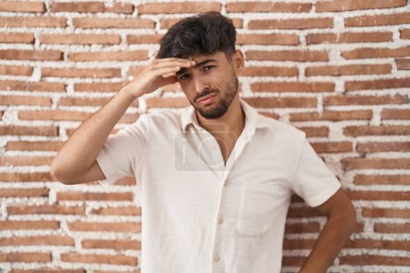 Photo for Arab man with beard standing over bricks wall background worried and stressed about a problem with hand on forehead, nervous and anxious for crisis - Royalty Free Image