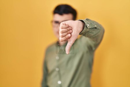 Foto de Non binary person standing over yellow background looking unhappy and angry showing rejection and negative with thumbs down gesture. bad expression. - Imagen libre de derechos